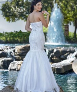 Woman in a strapless white mermaid gown stands by a pond with a fountain, facing away from the camera.
