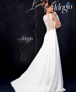 Woman wearing a sleeveless white wedding dress with a lace back and a long train, standing against a dark background.