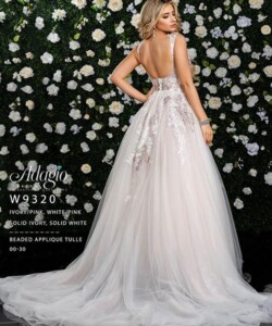 Woman wearing a beaded applique tulle gown with a low back, standing before a flower-covered wall.