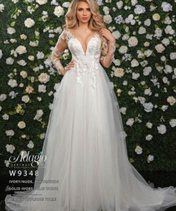 Woman in a white wedding gown with floral appliqués stands in front of a green wall decorated with white roses.