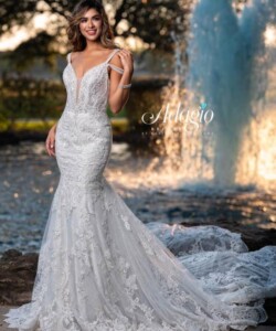 A woman in a white lace mermaid wedding dress poses outdoors near a fountain and greenery.