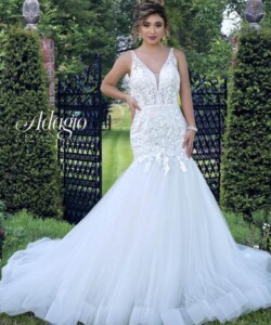Woman in a white lace mermaid wedding dress stands in front of open black iron gates in a garden.