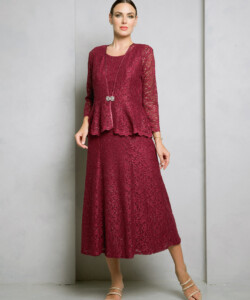 Woman wearing a burgundy lace three-piece dress with long sleeves, standing against a plain gray wall.